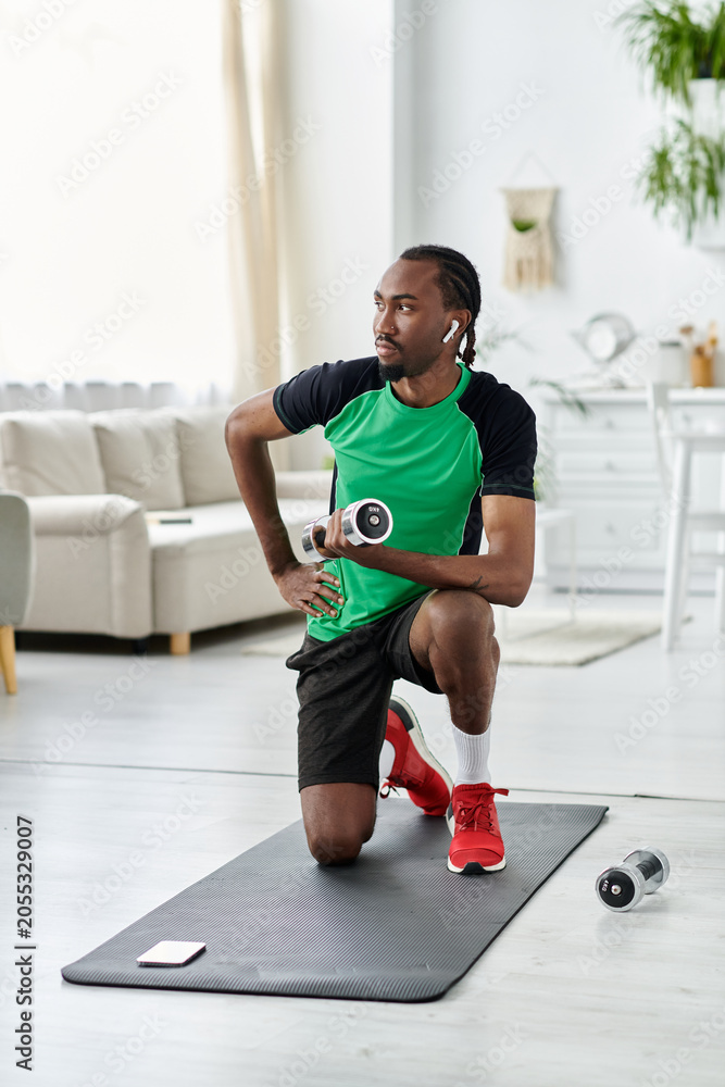 Fototapeta premium Young African American man exercising in a bright apartment while focusing on fitness and wellness