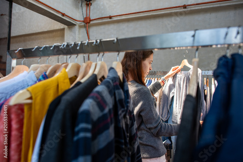 Foto Person browsing clothes on a rack in a store, wearing a gray sweater