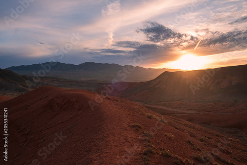 Sunset over the red clay mountains of Boguty in Kazakhstan. This scenic landscape with dramatic sky serves as a commercial background for travel websites, adventure lifestyle media, and copy space.