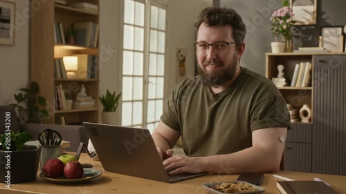 Portrait of middle aged Caucasian man with diabetes CGM sensor on arm typing on laptop at home and smiling. Footage ideal for diabetes awareness campaigns and digital health marketing