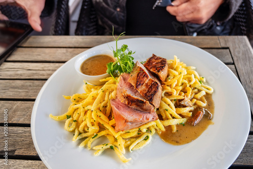 Roasted sliced tenderloin with pasta (spetzle) and mushroom sauce on white plate on table.