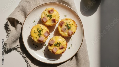 Overhead shot of four savory mini quiches with ham and parsley on a white plate and linen