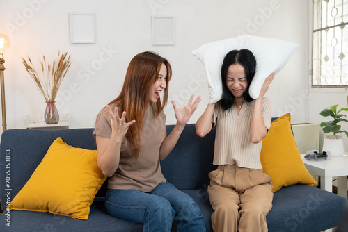 Asian women raising hands playfully after shouting conflict, symbolizing communication, stress, and lifestyle concept in cozy home environment with sofa, cushions, decorative plants