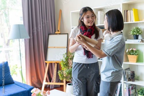 Asian siblings adjusting scarf in bright living room, highlighting family bonding, lifestyle connection, and everyday domestic affection with cozy couch, bookshelves, and natural daylight atmosphere