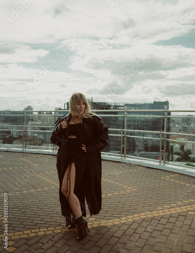 A girl in a black cloak poses on the roof of a building in the city