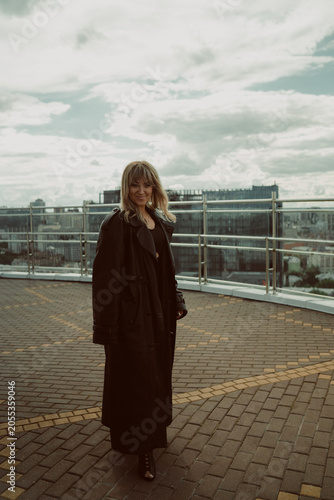 A girl in a black cloak poses on the roof of a building in the city