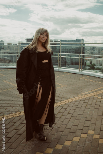 A girl in a black cloak poses on the roof of a building in the city
