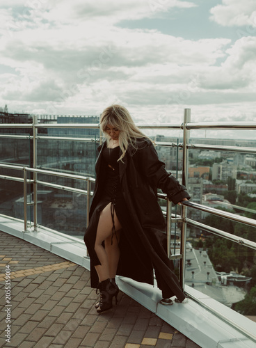 A girl in a black cloak poses on the roof of a building in the city