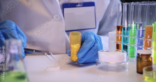 Doctor hands put pills into plastic bottle with tongs at desk in lab. Medical specialist packages innovative supplement for tests in laboratory
