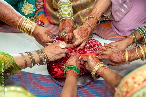 Indian women with intricate henna designs and bangles participate in a traditional ceremony