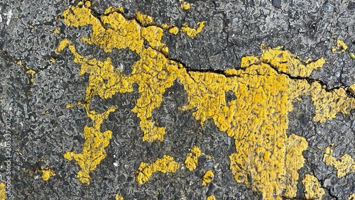 Cracked asphalt road surface with peeling yellow paint texture closeup