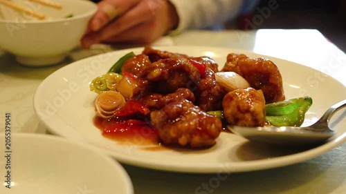 A person holding chopsticks and eating sweet and sour pork in a restaurant, slow motion
