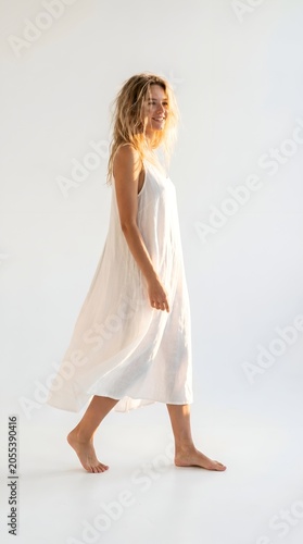 Happy young woman in a white dress walking against a bright studio background