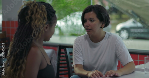 Fotografie Two women talk face to face at restaurant table, one responding seriously while