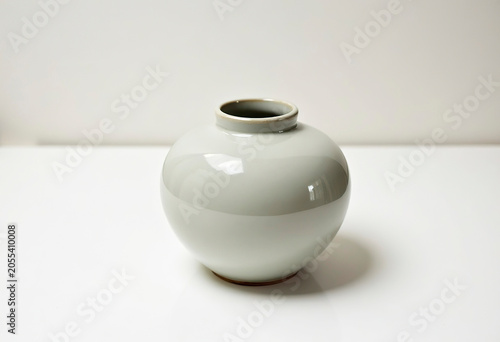 A grey round ceramic vase with a narrow neck on a white table, a place for text.