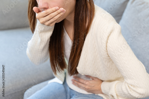 Canvastavla Close-up of young Asian woman covering mouth and holding her stomach in pain, nausea or morning sickness symptom concept