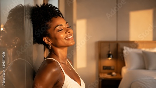A woman leans against a window in a softly lit, warm-toned room, eyes closed with a calm smile, bathed in sunlight during the late afternoon with interior decor