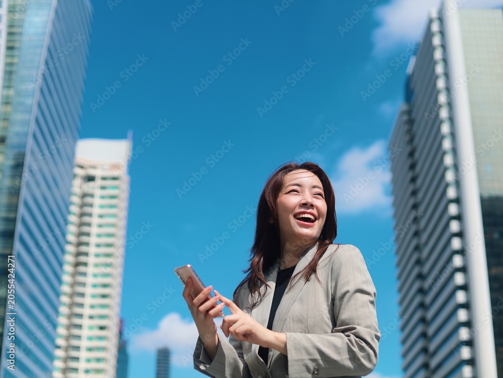 Fototapeta premium Confident young Asian businesswoman smiling outdoors in a modern urban environment with office buildings in the background.