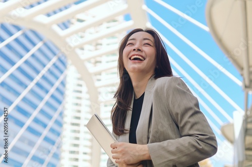 Confident young Asian businesswoman smiling outdoors in a modern urban environment with office buildings in the background.