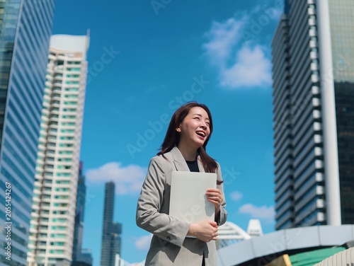 Confident young Asian businesswoman smiling outdoors in a modern urban environment with office buildings in the background.