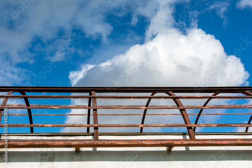 Rusty metal railing against a blue sky with clouds.