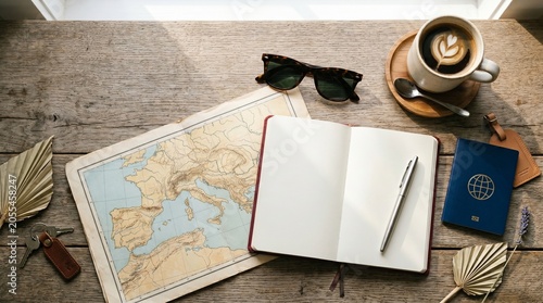 Open blank notebook with a pen, vintage map of Europe, passport, and coffee cup on a rustic wooden table. Travel planning and itinerary concept.
