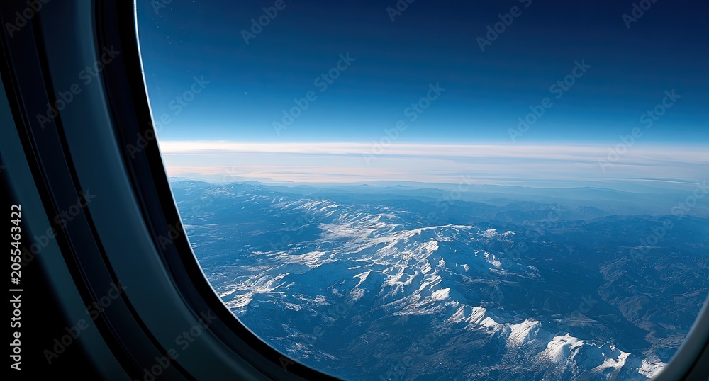 Fototapeta premium View from airplane window of sunlit snow-capped mountains beneath vast blue sky