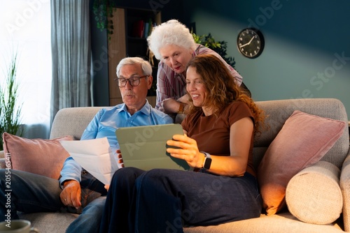Adult daughter helping elderly parents use tablet to pay household bills online. Digital banking, family support and financial literacy concept.