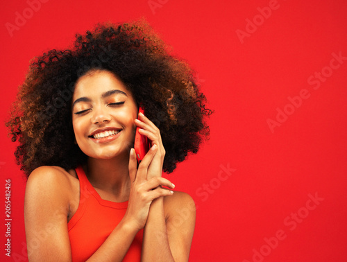 Studio portrait of biracial young woman with red smartphone and afro-textured hair