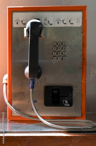 Vintage public payphone with an orange frame and black handset