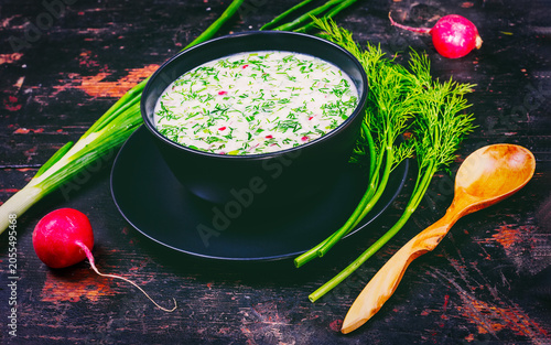A refreshing bowl of homemade okroshka, featuring finely chopped vegetables, boiled eggs, ham or sausage, and fresh herbs, dressed with cold kvass or kefir for a traditional summer meal