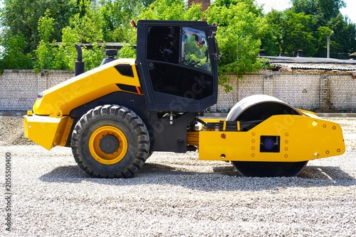 A bright yellow road roller displayed at a construction site. This heavy machinery is positioned on gravel, suitable for industrial use on infrastructure projects and roadworks