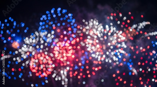 Bokeh of red white and blue fireworks illuminating night sky over celebration.