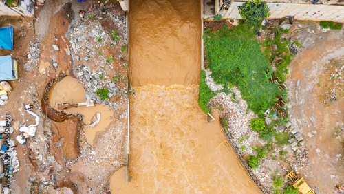 Fotografija Aerial view, Muddy floodwaters rushing through an overflowing storm drain in acc