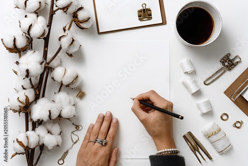 Woman writing on blank paper next to cotton flowers and coffee