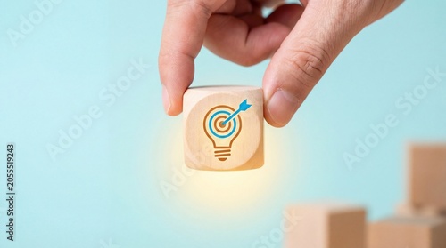 Hand placing wooden block with light bulb and target icon on building blocks, highlighting lightbulb and stack elements for modern business and office