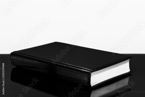 A closed black book on a black table on a white background with a copy space