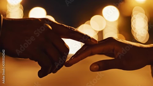 Close-up of two hands reaching out touching fingertips blurred golden bokeh lights background
