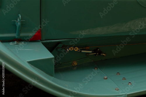 Detailed close-up view of a light green aircraft wing flap area showing metal panels, exposed mechanical linkage, hinge components and flush rivets. Soft