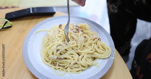 Hungry man carefully twirls creamy carbonara around silver fork at table. Male enjoys rich aroma of freshly prepared Italian dish. Slow motion