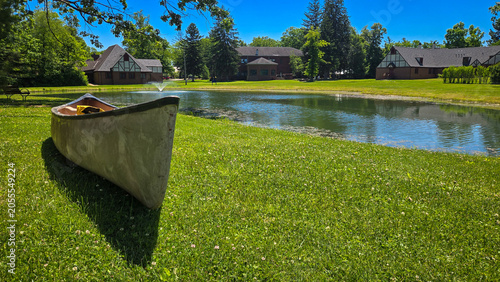 Canoe on grassy shore by a pond near historical campus buildings