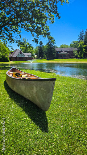 Canoe resting on green grassy shore near park pond and buildings