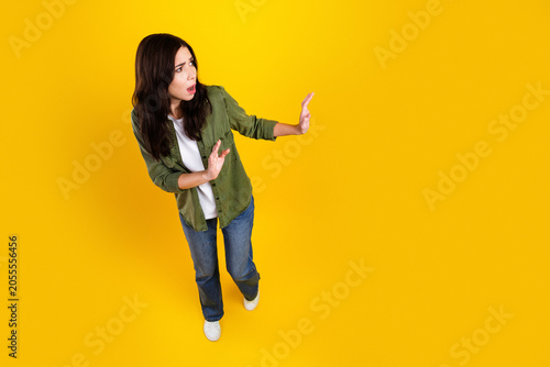 Tableau sur toile Young woman looking surprised and defensive on bright yellow background, backing