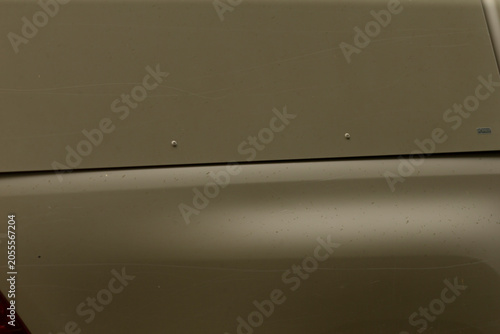 Close-up view of an olive green car trunk and rear panel showing metal surface with subtle reflections, small rivets, panel seams, and faint surface