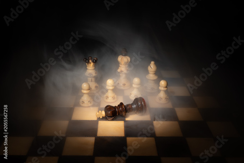 Bild auf Leinwand Dark chess king fallen on chessboard among white pieces in dramatic smoke