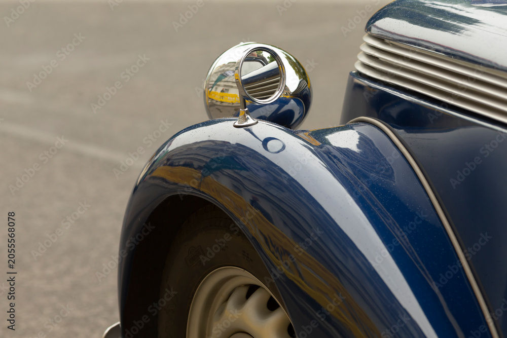 Fototapeta premium Detailed close-up of the front left fender and round headlight of a glossy blue vintage car. Visible features include chrome headlight housing, curved metal