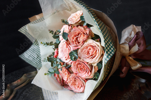 Bouquet of blush peach David Austin-style roses wrapped in kraft and gingham paper with eucalyptus, black background - romantic gift floral shot