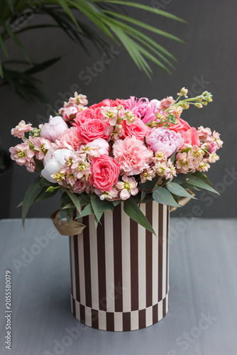 Floral arrangement with coral roses, peonies, carnations and stock in striped black-and-white hat box on gray surface - chic flower gift box shot