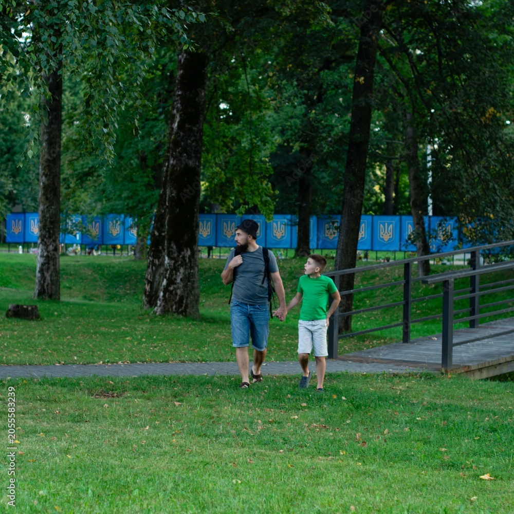 Fototapeta premium A father and son stroll through a park, enjoying a leisurely afternoon together.