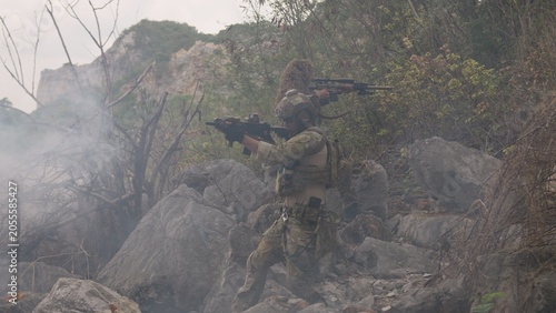 Tableau sur toile A special forces team conducts a tactical operation in a rocky, smoky environment, with a sniper providing covert surveillance from an elevated position